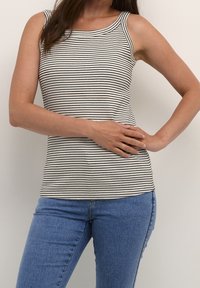 Gestreifter Tanktop aus schwarz-weißer Rippstoff, mit rundem Halsausschnitt und figurbetonter Passform. Kombiniert mit blauen Jeans.
