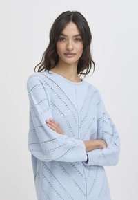 Himmelblaues Strickoberteil mit Rundhalsausschnitt, langen Puffärmeln und einem strukturierten Muster aus diagonalen Lochmusterausschnitten.