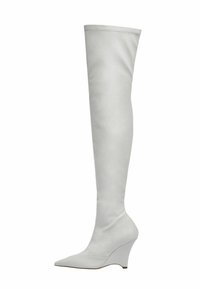 Bota blanca por encima de la rodilla hecha de cuero suave, con punta afilada y tacón en cuña. La costura en la parte superior añade un sutil acento.