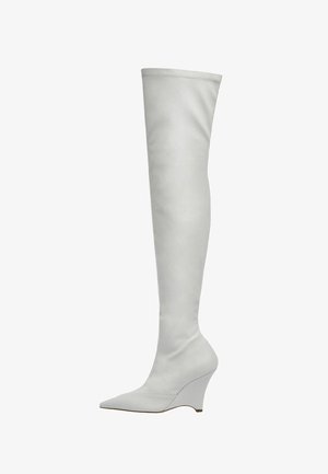 Białe kozaki za kolano wykonane z gładkiej skóry, z wydłużonym noskiem i koturnem. Szycia wzdłuż cholewki dodają subtelnego akcentu.