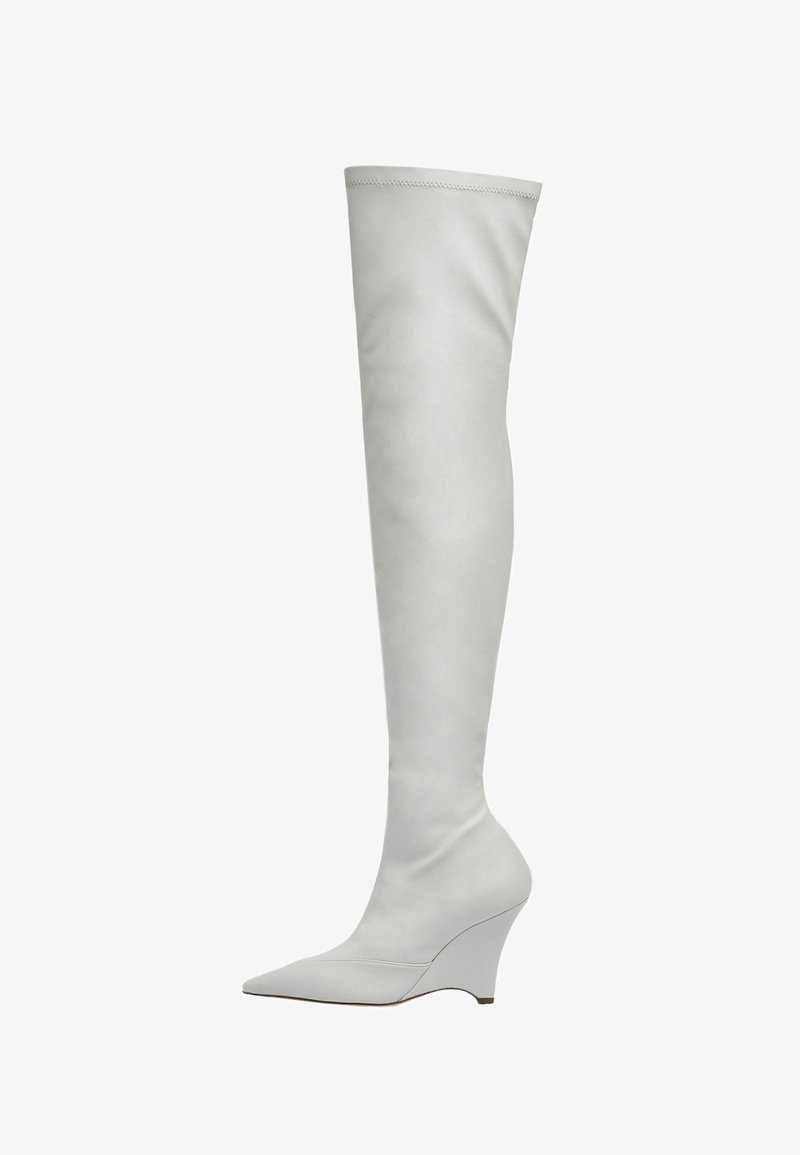 Białe kozaki za kolano wykonane z gładkiej skóry, z wydłużonym noskiem i koturnem. Szycia wzdłuż cholewki dodają subtelnego akcentu.