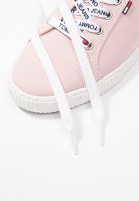 Ljusrosa canvas-sneakers med vit gummisula. Har vita snören, en märkt textil-flik och metallöglor för snörning.