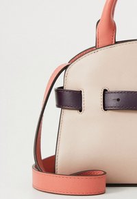 Usnjena torbica v bež barvi z vijoličnim trakom in breskovo poudarkom. Ima strukturirano obliko in gladko teksturo z minimalno kovinsko opremo.