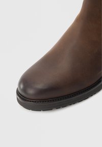 Hnědá kožená bota s kulatou špičkou, prošitým detailem podél podrážky a texturovanou gumovou podrážkou pro lepší přilnavost.