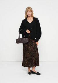 Cardigan preto de malha com decote em V e botões, combinado com uma saia maxi de padrão de leopardo. Sapatilhas pretas e uma mala escura completam o conjunto.