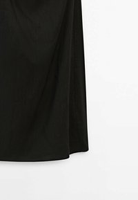 Robe noire en tissu léger, présentant une coupe droite, une fente sur le côté, et une texture subtile avec une finition lisse.