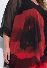 Czarna tunika z dużym czerwonym wzorem maku, wykonana z przezroczystej, lekkiej tkaniny, z luźnymi rękawami i okrągłym dekoltem.