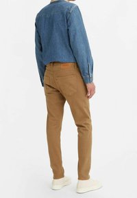 Vaate denim-takkia vaaleansinisenä, khaki-housuja takataskuilla ja kerma-valkoisia lenkkareita. Mukana nahkainen merkki vyötäröllä.