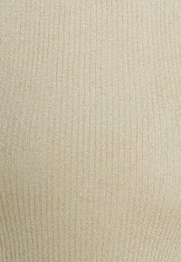 Gros plan sur un tissu beige en maille côtelée avec un léger scintillement et des lignes texturées verticales.