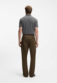 Graues Polohemd mit kurzen Ärmeln, kombiniert mit braunen Hosen. Der Stoff des Outfits wirkt glatt, mit einer lockeren Passform und zwei Gesäßtaschen.