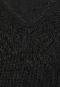 Svart stickad tyg med en V-formad spetsdetalj längs halslinningen, som visar texturerad sömnad och ett fint spetsmönster.