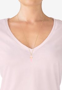 Gul kæde med en pink vedhæng, der har et låsdesign. Båret med en lys pink V-hals t-shirt. Enkel og elegant.