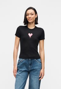 Camiseta negra ajustada de manga corta, con un gráfico de corazón rosa en el centro. El material parece suave, con un diseño clásico de cuello redondo.