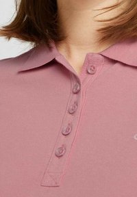 Rosa Poloshirt mit einem Kragen, einer Knopfleiste mit fünf Knöpfen, strukturiertem Stoff und einem dezenten Logodetail an der Seite.