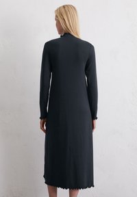 Czarna sukienka z długim rękawem, wykonana z miękkiego materiału, z wysokim dekoltem oraz falbaniastym dołem i mankietami, sięgająca do połowy łydki.