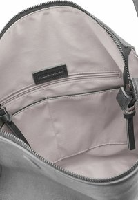 Intérieur d'un sac à main en tissu gris avec doublure douce. Comprend une poche zippée, une étiquette de marque et des bretelles ajustables.