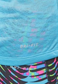 Modrý sportovní top z materiálu Dri-FIT odvádějícího vlhkost, s texturovaným potiskem a černým spodním dílem s živými, vícerozměrnými abstraktními vzory.