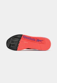 Reebok kurpes zole ar spilgtu sarkanu un melnu gumijas dizainu, kas ietver teksturētus rievojumus un Reebok logo zilā krāsā.