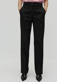 Svarta randiga byxor med en slät textur, med hög midja och sidofickor. I kombination med spetsiga svarta skor.