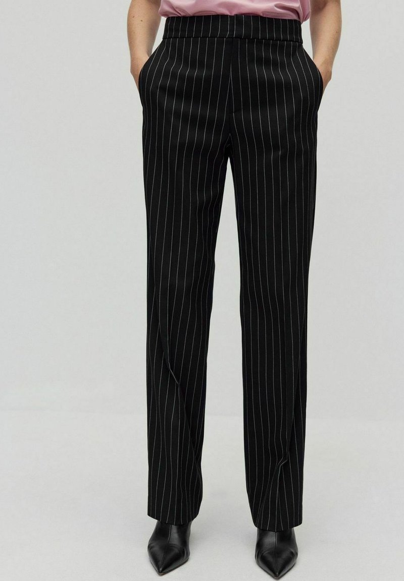 Svarta randiga byxor med en slät textur, med hög midja och sidofickor. I kombination med spetsiga svarta skor.