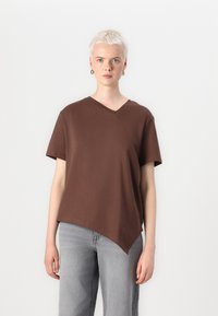 Brun bomull T-skjorte med V-hals, asymmetrisk kant og korte ermer. Kombinert med lysegrå vide jeans.