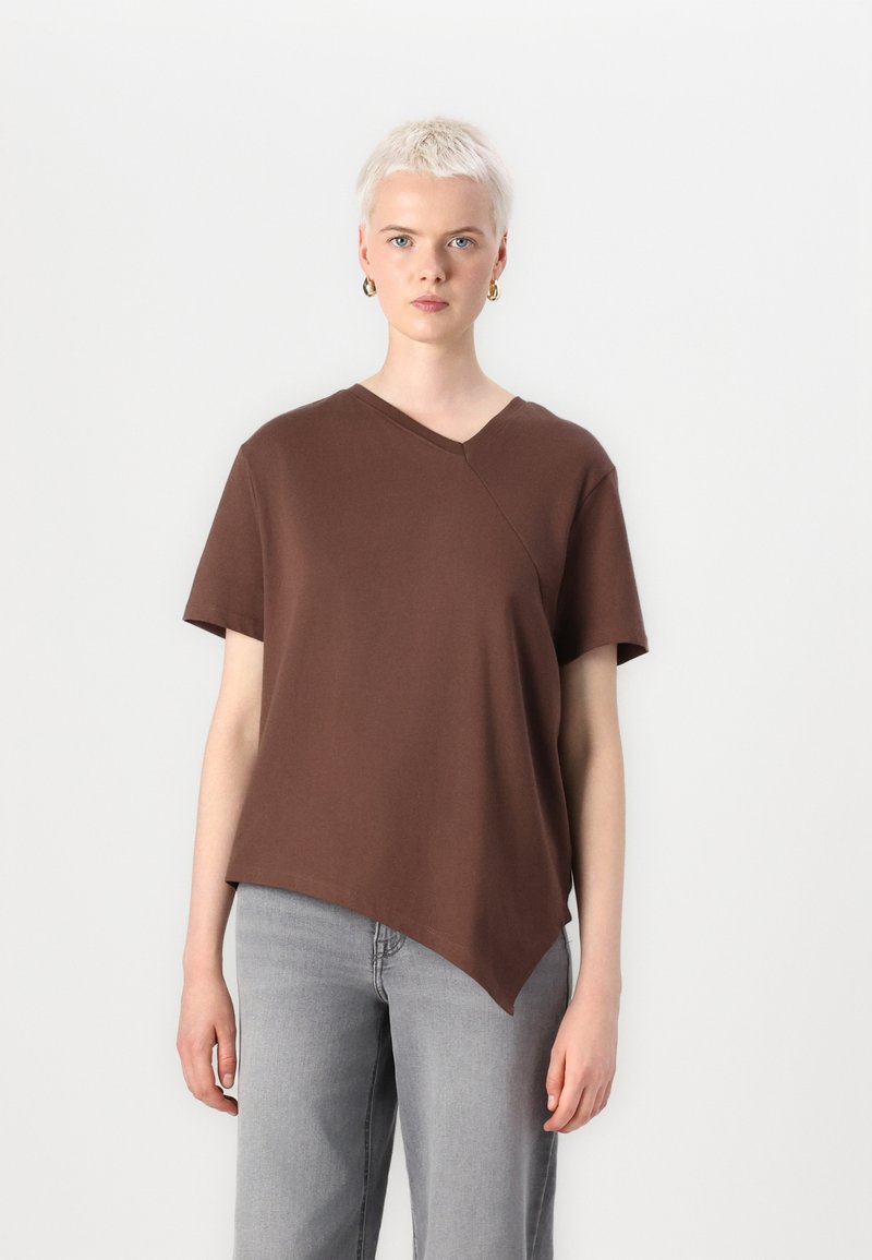 Brun bomull T-skjorte med V-hals, asymmetrisk kant og korte ermer. Kombinert med lysegrå vide jeans.