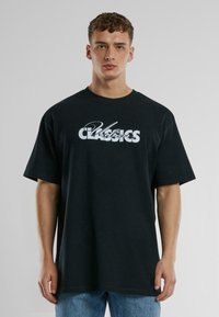 Juodas per didelis medvilnės marškinėliai su ryškiu baltu užrašu "Urban Classics" stilizuotu šriftu krūtinės srityje.