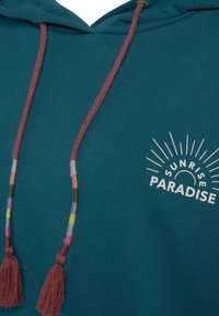 Felpa blu petrolio con una grafica frontale che recita "SUNRISE PARADISE." Presenta un cordino bordeaux con perline colorate e nappine.
