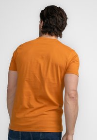 Camiseta de manga corta de algodón de color naranja brillante, diseño ajustado con cuello redondo, textura lisa y sin gráficos ni acentos visibles.
