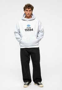 Grijze hoodie met de print "POLIZEI 15594", kangoeroe-pocket, gecombineerd met zwarte wijde broek en zwarte sneakers met witte veters.