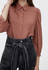 Dusty rose button-up shirt with puffed sleeves, paired with high-waisted, dark denim jeans featuring a tie belt and contrasting stitching.