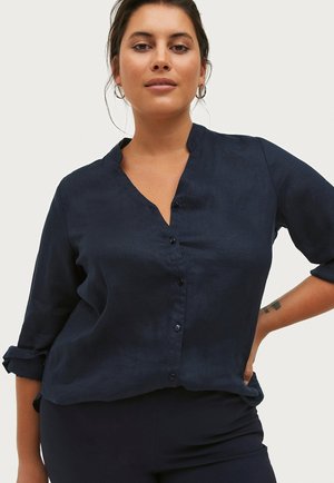 Camicia button-up in lino blu navy con colletto a incastro, maniche lunghe arrotolate e vestibilità rilassata. Dotata di bottoni frontali e una texture liscia.