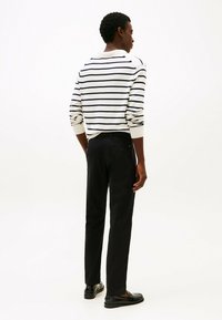 Maglione a righe in bianco sporco e blu navy, con polsini a costine. Abbinato a pantaloni neri. Modello mostrato di spalle, in una posa casual.