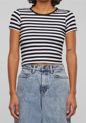Buste d'une personne portant un t-shirt à manches courtes rayé horizontalement noir et blanc et un jean en denim bleu clair taille haute avec un tatouage "MAYBE" sur le bras gauche.