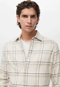 Beige karierte Button-up-Bluse aus weichem Stoff, mit einem kragenlosen Halsausschnitt und einem lässigen, lockeren Schnitt. Knöpfe und Karomuster sind sichtbar.