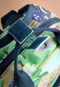 Večbarvni nahrbtnik z vzorcem zelenega in modrega gozda, temno modrimi naramnicami, zadrgo ter velcro zanko.