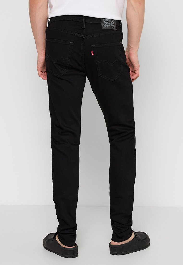 Black denim jeans with a slim fit, featuring a leather brand patch, two back pockets, and a red tab accent on the rear.