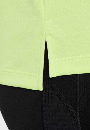 Bright lime green athletic shirt with side slits, layered over black fitted leggings featuring textured patterns at the waist.