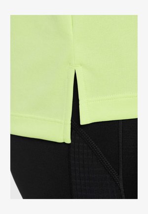Camisa deportiva de un vibrante verde lima con aberturas laterales, superpuesta sobre leggings ajustados negros que presentan patrones texturizados en la cintura.