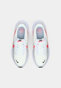 Balti tinkleliai bėgimo bateliai su rožiniais akcentais, apvaliu priekiu, raištelių užsegimu, paminkštintu liežuviu ir tekstūruota guma ant padų. Matomas Nike logotipas.