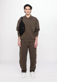 Καφέ βαμβακερή μπλούζα με γιακά, συνδυασμένη με καφέ φόρμα. Μαύρη τσάντα ώμου στο αριστερό ώμο. Λευκά αθλητικά παπούτσια.