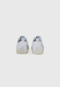 Lys grå suede sneakers med en teksturert gummisåle, polstret krage og trekkhanker bak på hælen. Subtil merking på baksiden.