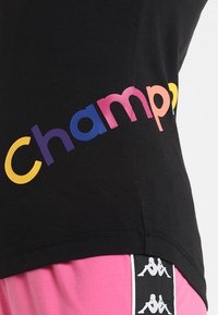 Černé tričko s vícebarevným nápisem "champ". Měkká tkanina, přiléhavý střih, s lemem a sousedícími růžovými šortkami s logem.