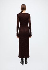 Long, fitted burgundy dress made of lace, featuring long sleeves and a round neckline, with a smooth texture and below-the-knee length.