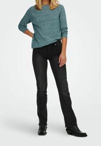 Tealfarbener strukturierter Pullover mit langen Ärmeln, kombiniert mit schwarzen, eng anliegenden Jeans und schwarzen, hochhackigen Stiefeln. Einfaches, modernes Design ohne Muster.