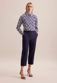 Long-sleeve shirt with a blue and white geometric pattern, paired with navy tailored trousers and black strappy sandals.