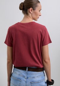 T-shirt en coton rouge à manches courtes et coupe décontractée, avec un col arrondi et une couture visible à l'arrière. Porté avec un jean taille haute.