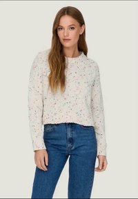 White knitted sweater with multicolored speckles, crew neckline, and cropped fit, paired with classic blue denim jeans.