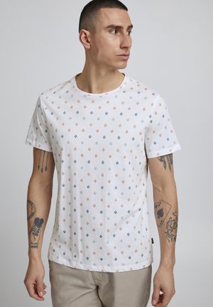 Witte katoenen t-shirt met een geometrisch patroon van kleine vierkantjes in oranje, groen, blauw en grijs. Korte mouwen en ronde halslijn.