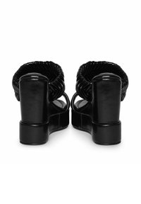 Sandalias negras de tacón con un diseño de parte superior trenzada, tacones gruesos y un acabado de cuero suave. Estilo destalonado y de punta abierta.